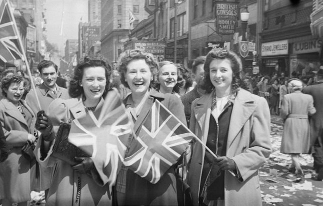 Three young women hold the Union Jack flag during VE Day celebrations on St. Catherine Street, Montreal